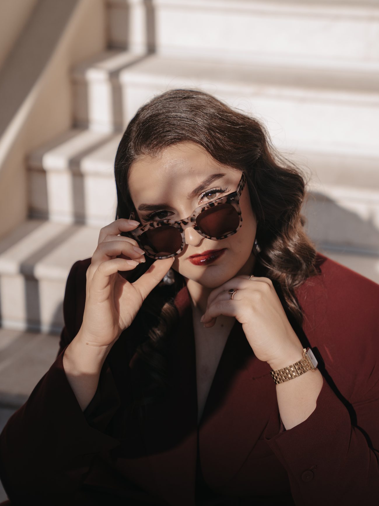Frederike Behrens sitzt im Sonnenlicht auf einer Treppe, schiebt ihre Sonnenbrille nach unten und blickt direkt in die Kamera.