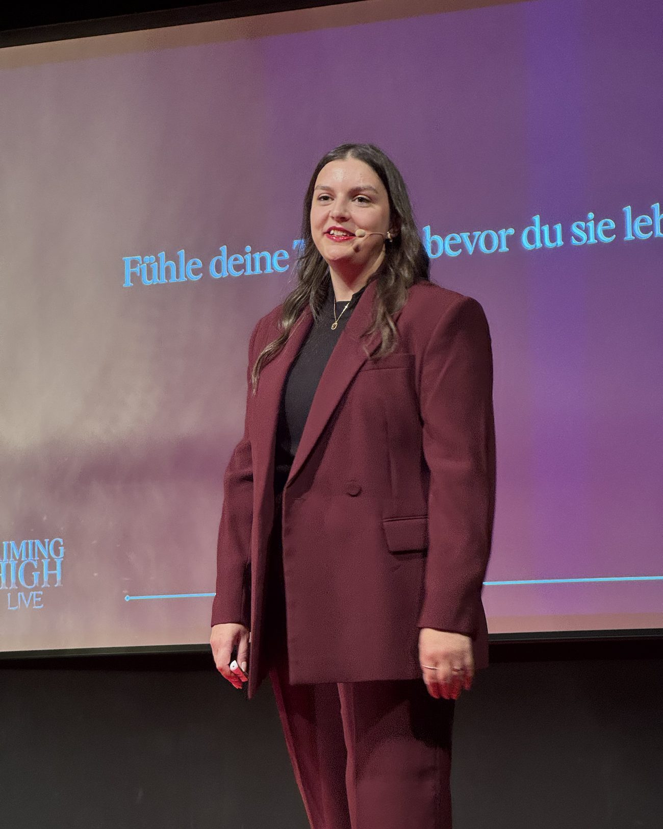 Frederike Behrens auf der Bühne mit Headset-Mikrofon vor einer großen Projektionsfläche.