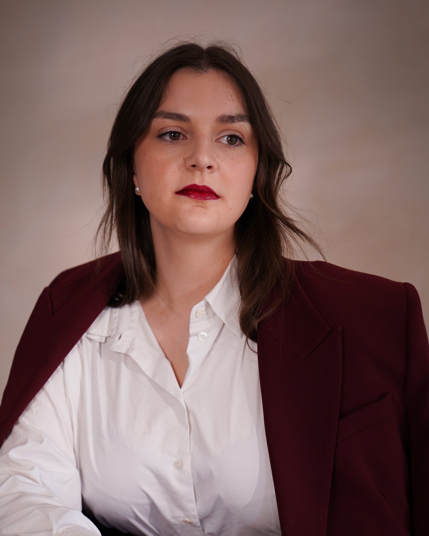 Frederike Behrens sitzt frontal zur Kamera, bordeauxfarbener Anzug über weißer Bluse.